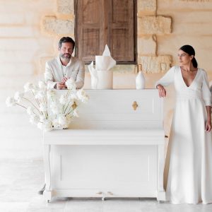 Piano ancien patiné crème transformé en bar, avec étagères de rangement intégrées pour verres et bouteilles.